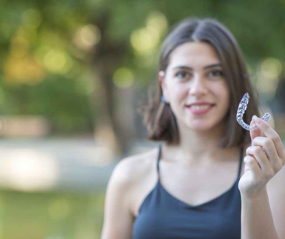 Woman holding a clear Invisalign aligner and smiling